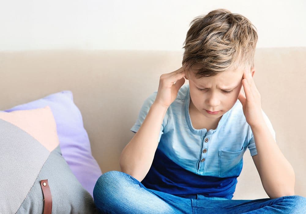 Barn sidder i sofa og tager sig til hovedet med rynkede øjenbryn