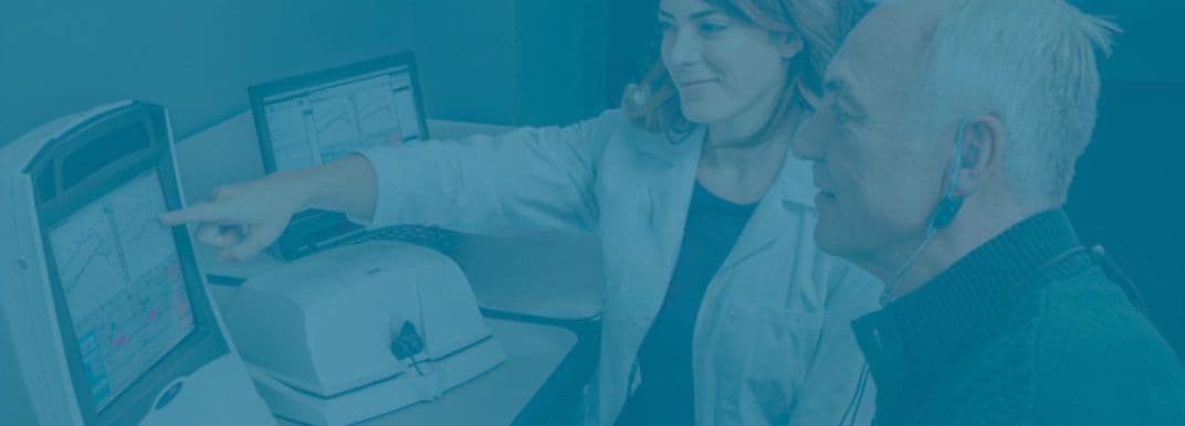 Kvindelig hørespecialist viser mandlig patient resultaterne af høreapparatstilpasningens binaurale måling på Audioscan Verifit2 skærmen.