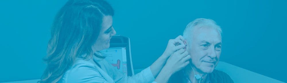 Kvindelig hørespecialist foretager en høreapparatstilpasning på en mandlig patient.